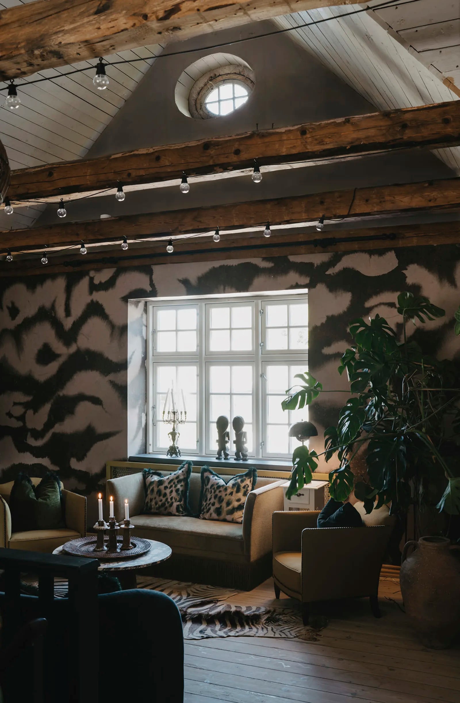 Guppy wall mural by Rebel Walls in muted brown tones, in a dim attic lounge with timber beams and green sofa