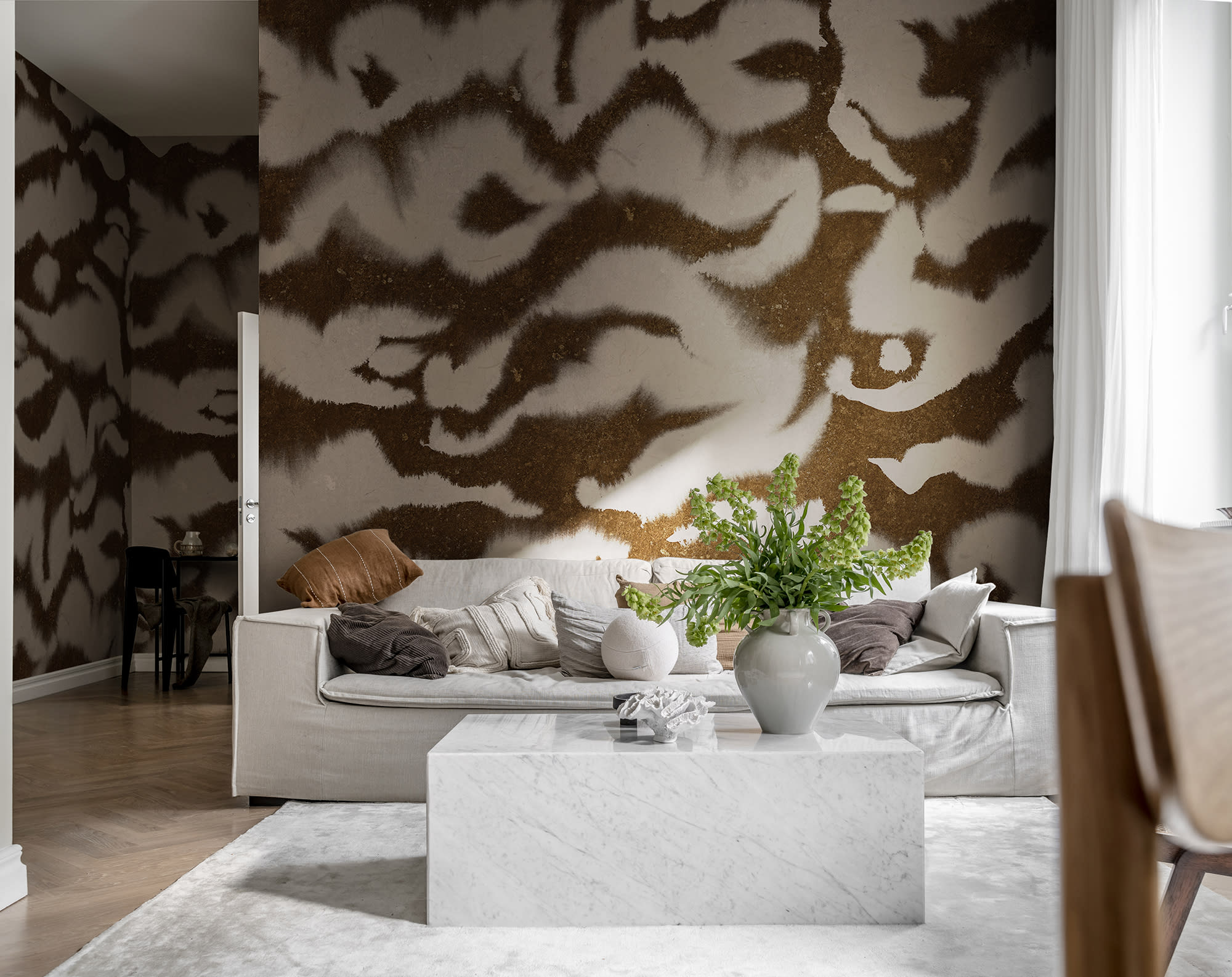 Guppy wall mural by Rebel Walls, brown and cream watercolour ikat swirls, styled in a living room behind a white sofa