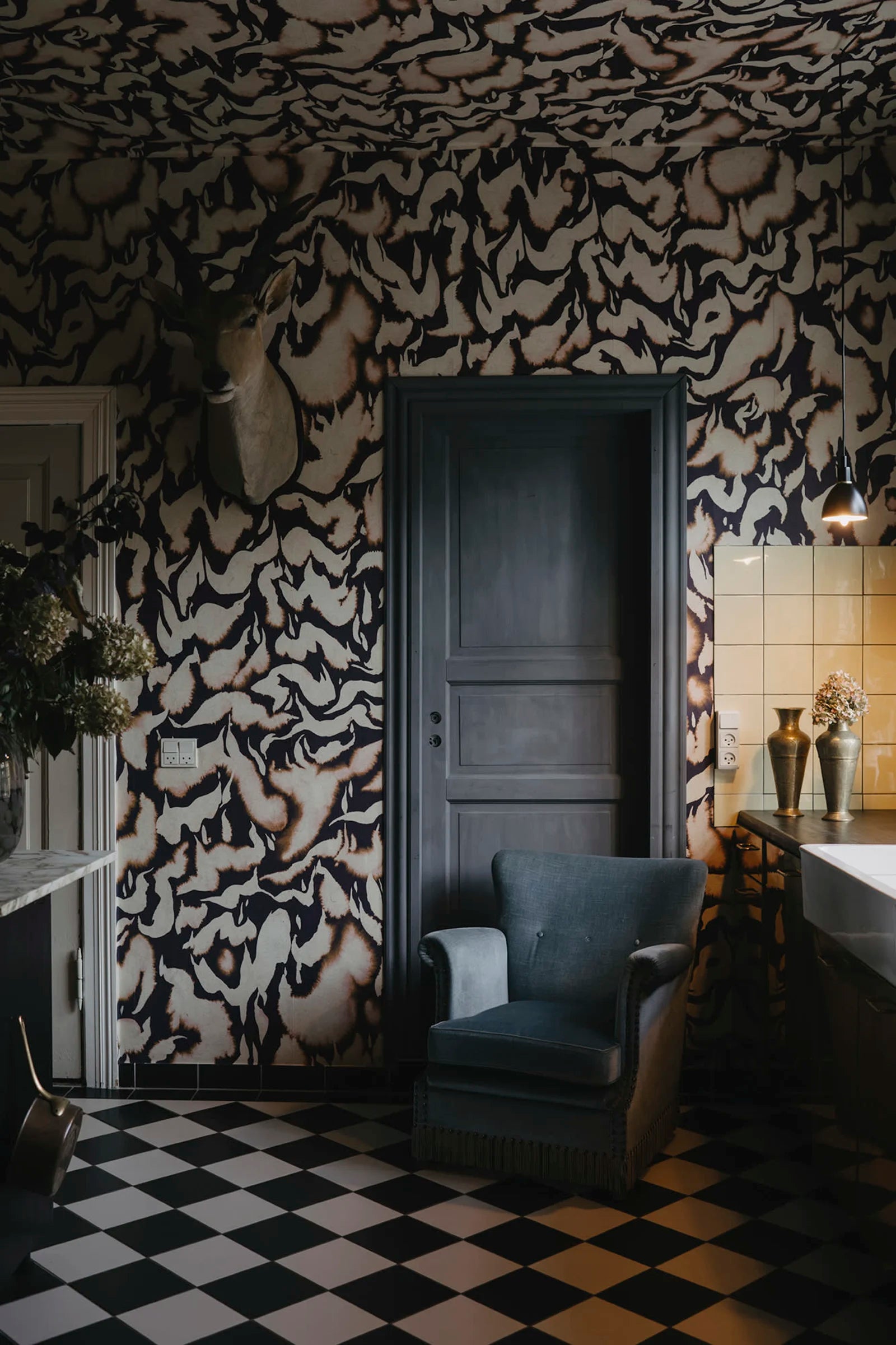 Discus Fish wall mural by Rebel Walls in plum and cream swirls, behind a grey door and velvet armchair on checkerboard floor