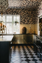 Discus Fish wall mural by Rebel Walls in plum and cream swirls on walls and ceiling of a kitchen with brass cabinets