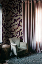 Discus Fish wall mural by Rebel Walls in plum and cream swirls, beside long curtains and a grey velvet armchair