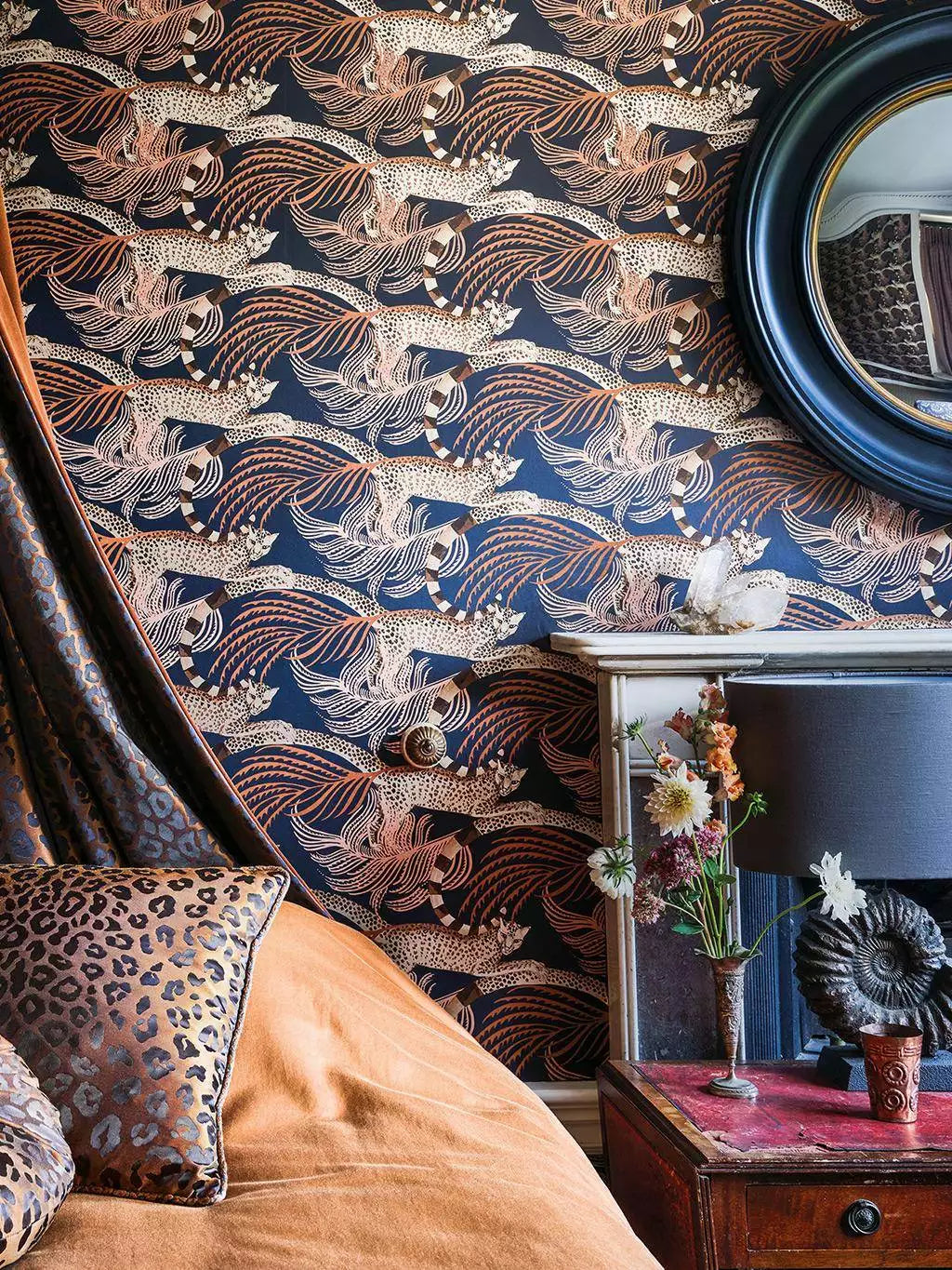 Delilah wallpaper by Romo in Blue - animals design, plumed birds in indigo behind an oval mirror and a leopard-print cushion