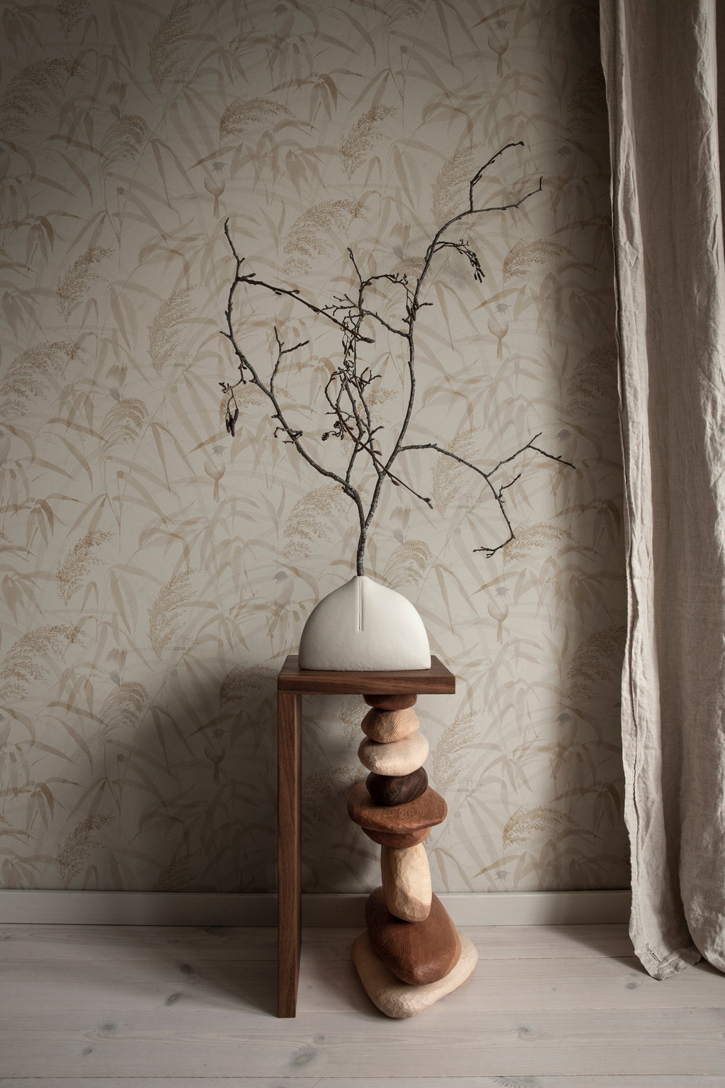 Anna wallpaper by Sandberg in beige close-up behind a sculptural vase with bare branches on a wooden stand