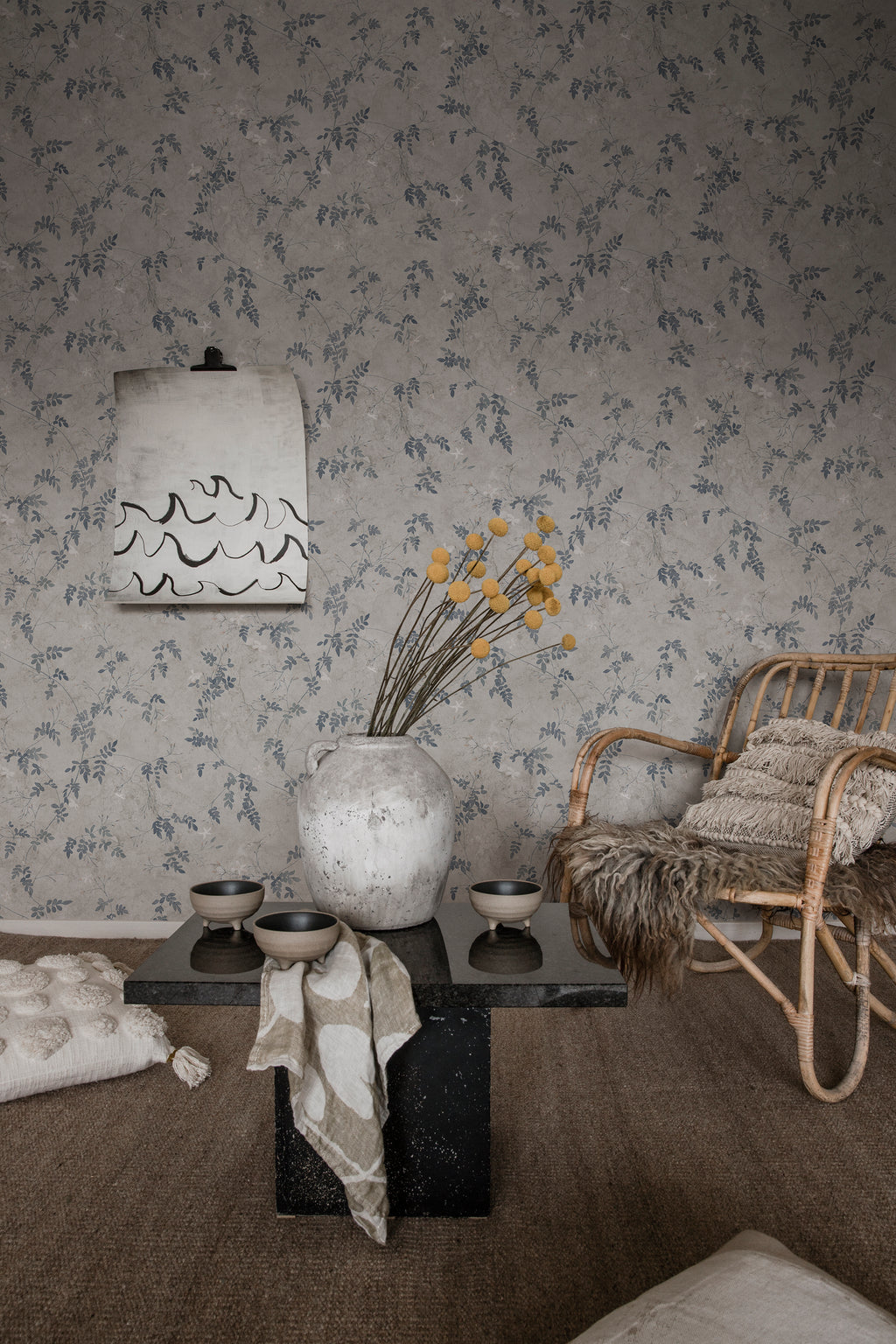 Irene wallpaper by Sandberg in blue-grey, in a living room with rattan chair and stone coffee table