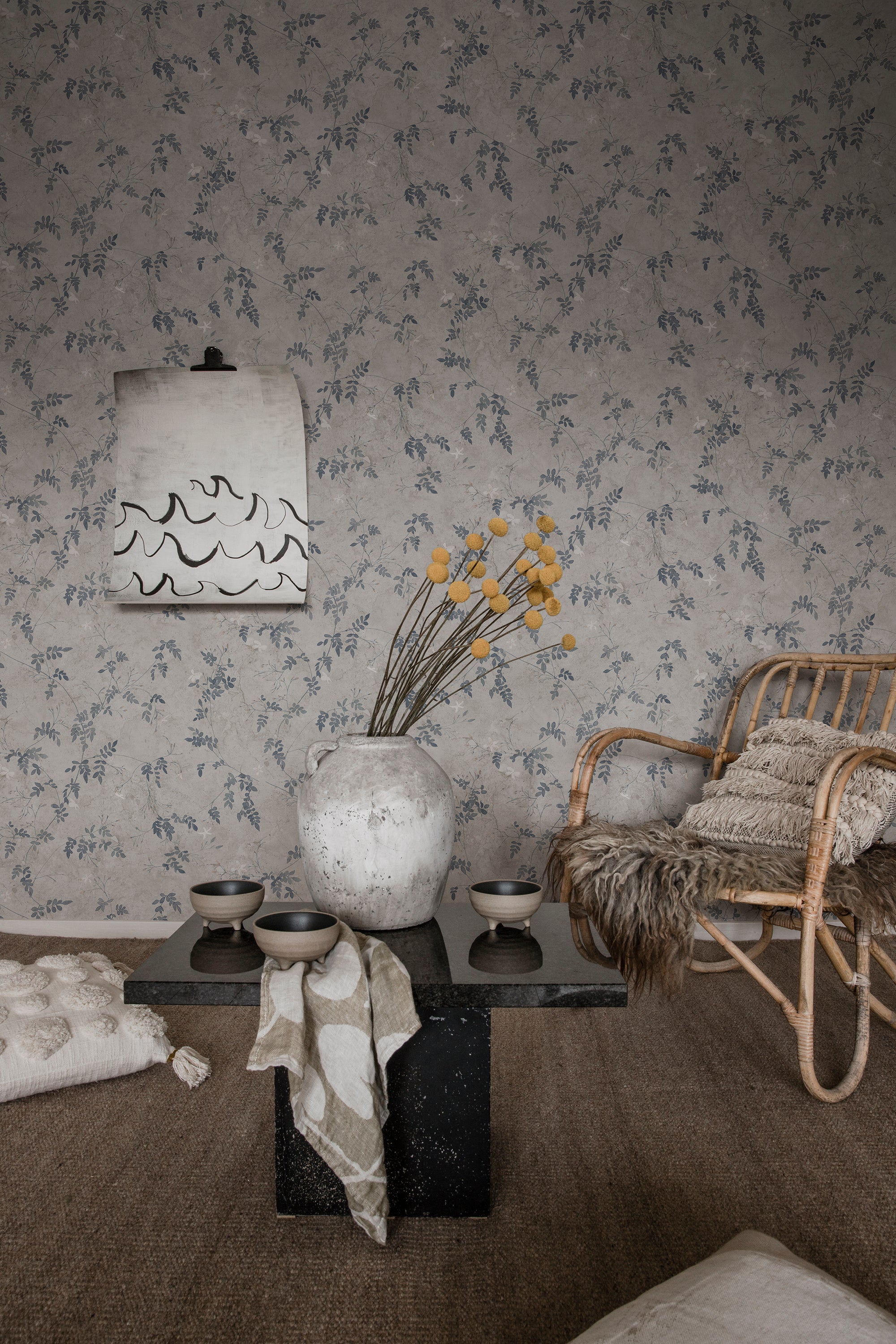Irene wallpaper by Sandberg in blue-grey, in a living room with rattan chair and stone coffee table