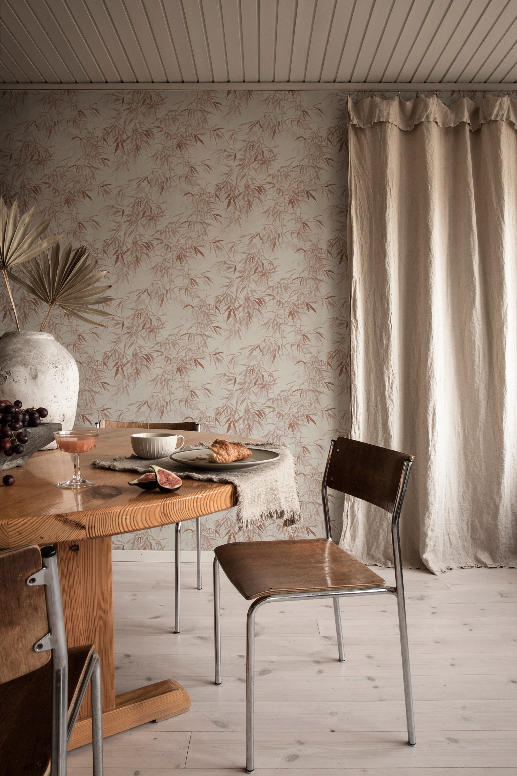 Jon wallpaper by Sandberg, terracotta bamboo-leaf print in a dining room with a wooden table and linen curtain