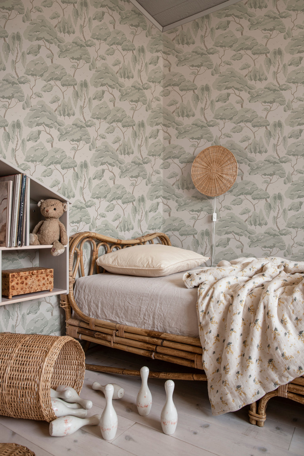 Kristoffer Forest tree wallpaper by Sandberg in soft sage above a rattan childrens daybed with teddy and skittles