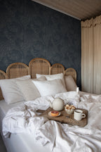 Evelina wallpaper by Sandberg in dark blue behind a bed with a rattan headboard and breakfast tray