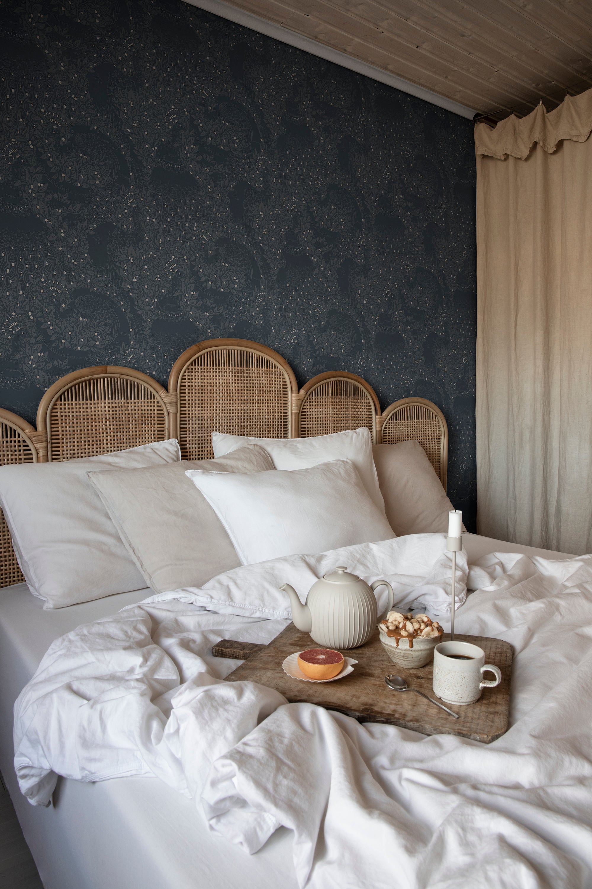 Evelina wallpaper by Sandberg in dark blue behind a bed with a rattan headboard and breakfast tray