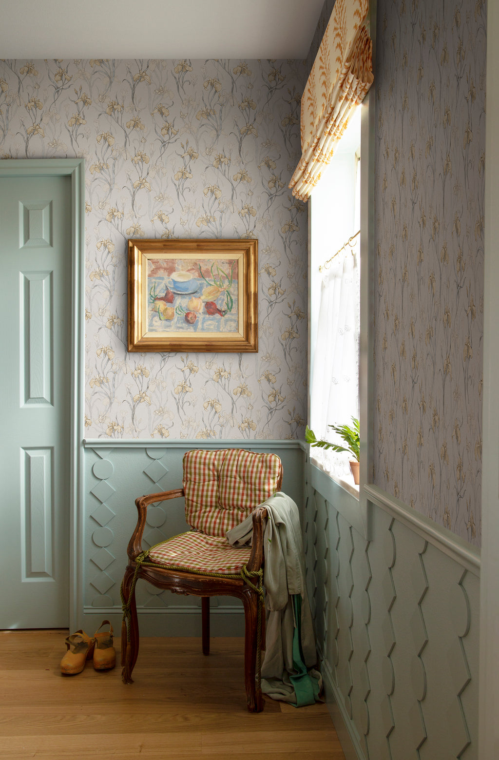 Iris wallpaper by Sandberg above pale wainscoting in a hallway with a gilt-framed painting and a gingham-cushioned antique chair