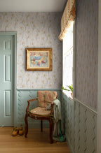 Iris wallpaper by Sandberg above pale wainscoting in a hallway with a gilt-framed painting and a gingham-cushioned antique chair