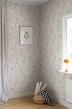 Iris wallpaper by Sandberg in soft gold styled in a corner with a framed botanical print, mustard lamp and rolled wallpaper in a basket