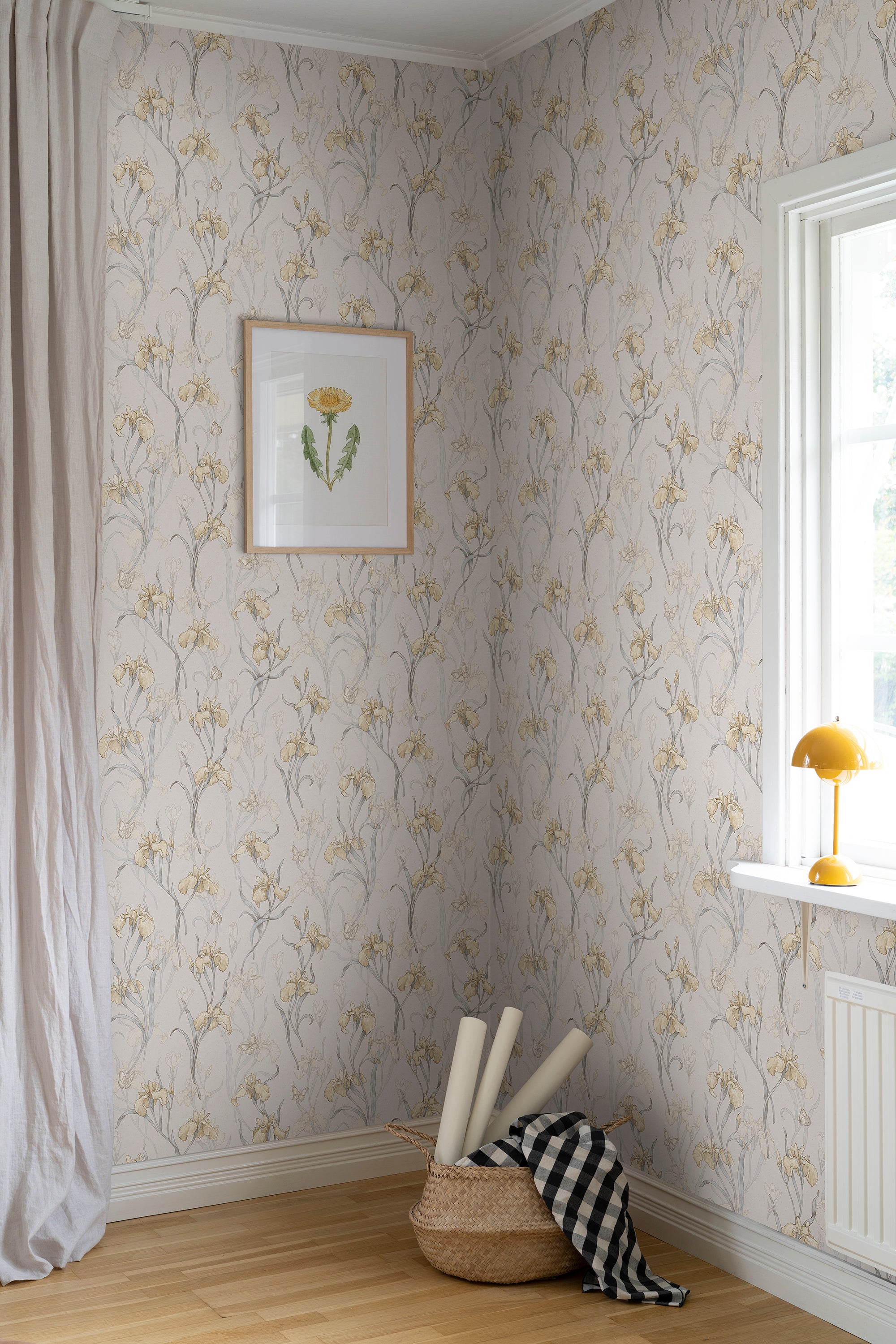 Iris wallpaper by Sandberg in soft gold styled in a corner with a framed botanical print, mustard lamp and rolled wallpaper in a basket