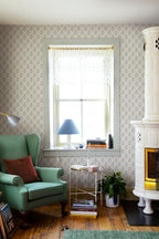 Maskrosen wallpaper by Sandberg in a cosy reading corner with a green wingback chair, tiled stove and lace-blind window