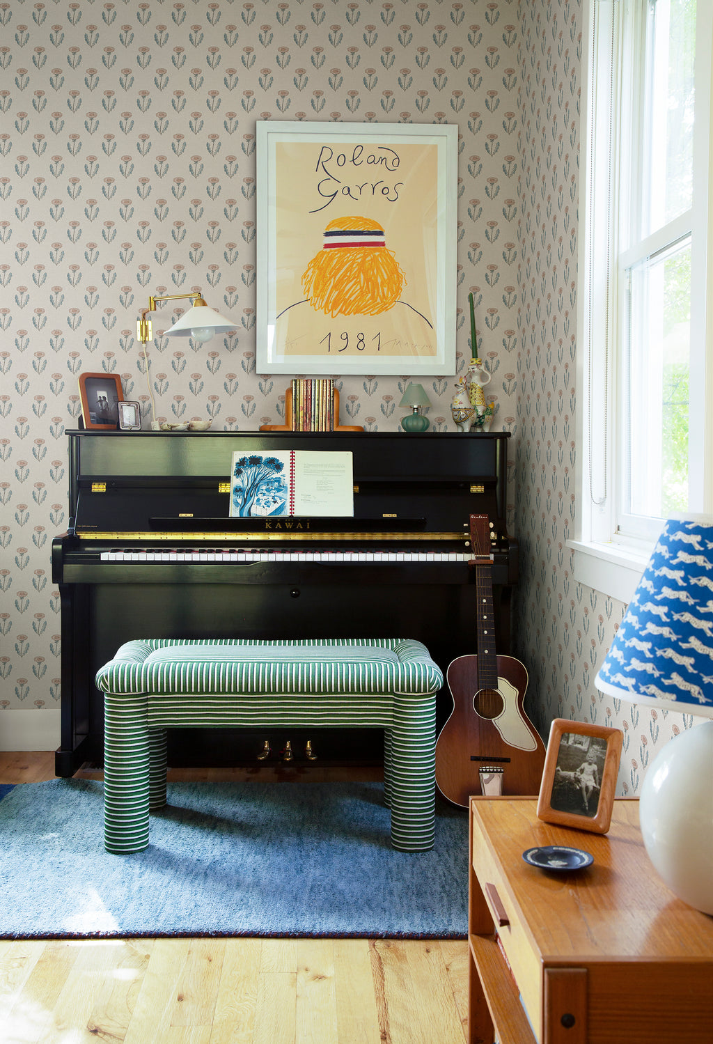Maskrosen wallpaper by Sandberg behind an upright piano with framed art, striped stool and guitar in a styled room