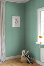Brita Stripe wallpaper by Sandberg in green, styled in a corner with framed botanical print, basket and yellow lamp