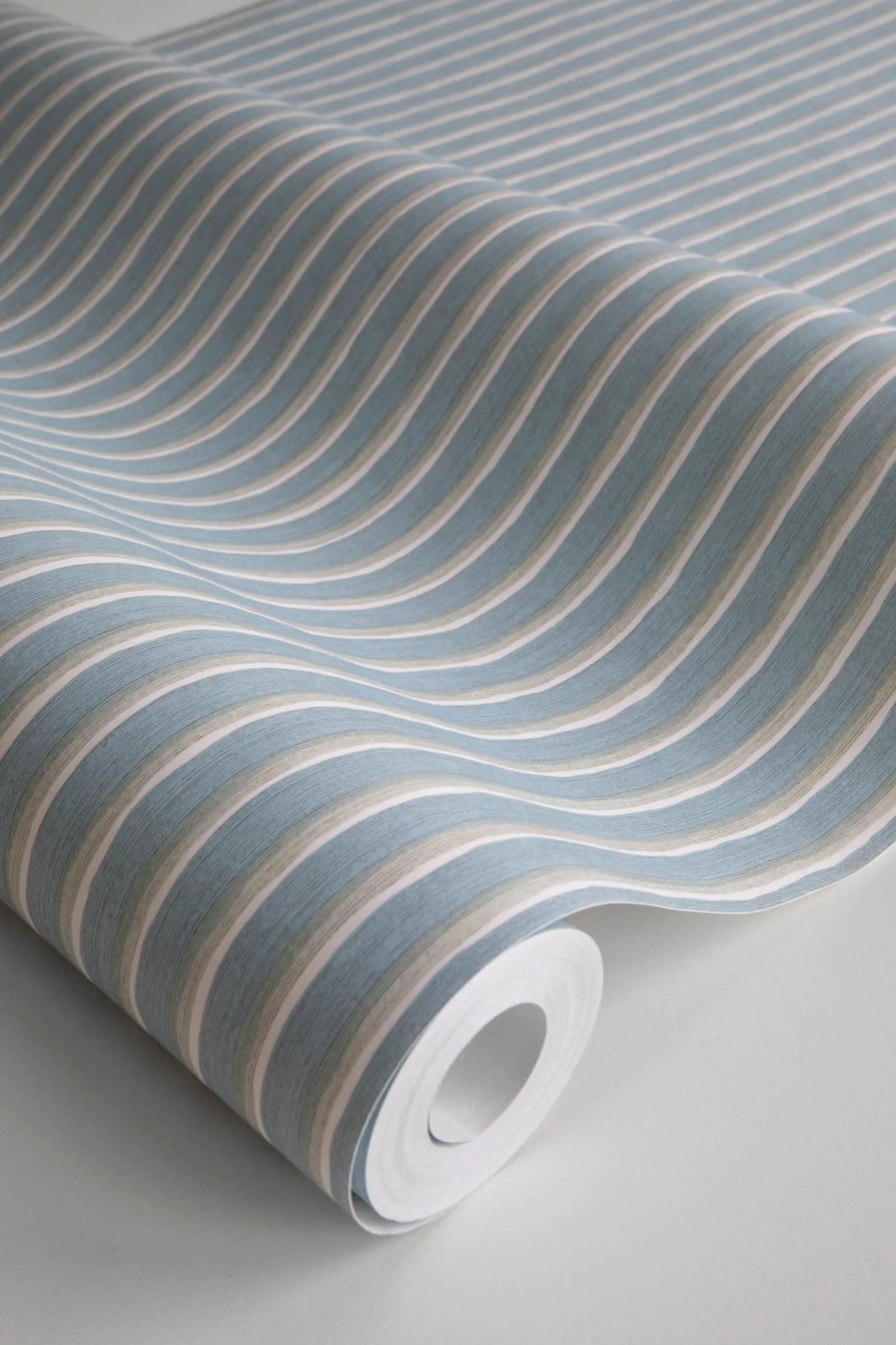 Brita Stripe wallpaper by Sandberg in blue, close-up of a wallpaper roll showing fine painterly vertical stripes