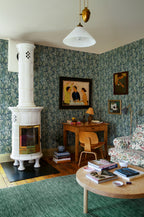 Kersti wallpaper by Sandberg, green chestnut-leaf print in a cosy living room with a white tiled stove and green rug