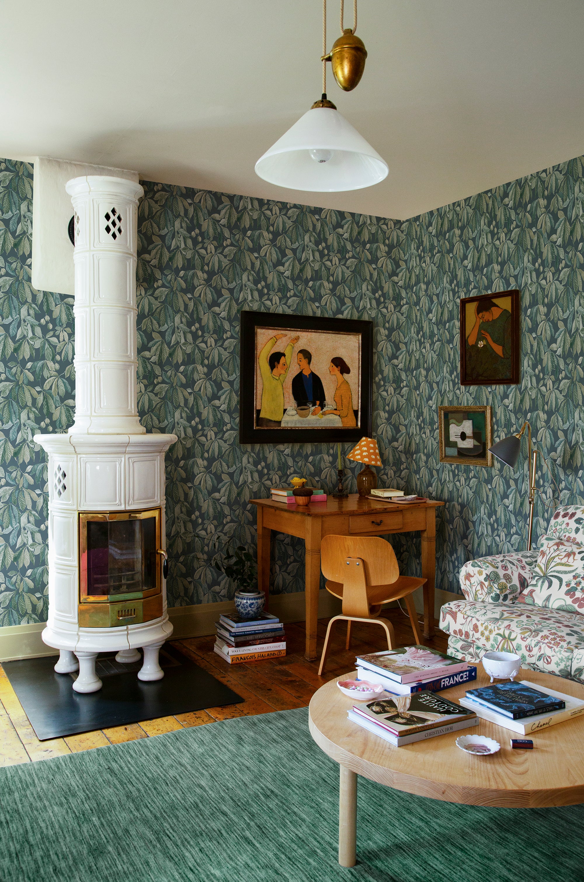 Kersti wallpaper by Sandberg, green chestnut-leaf print in a cosy living room with a white tiled stove and green rug