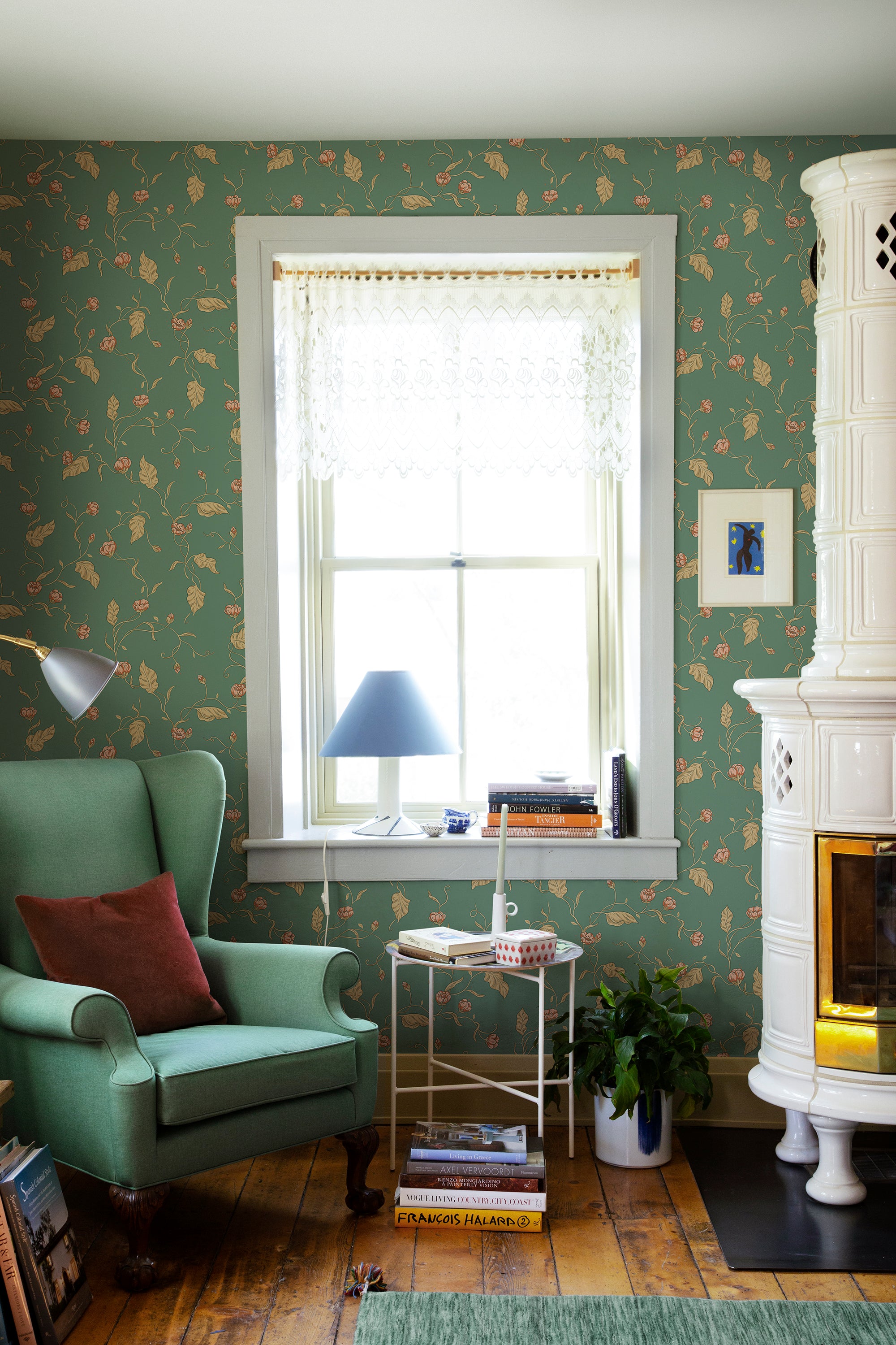 Elmire wallpaper by Sandberg in green in a cosy reading corner with a green wingback chair and tiled stove