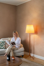 Terracotta Lyckan wallpaper by Sandberg in a sitting room with a woman reading beside a floor lamp