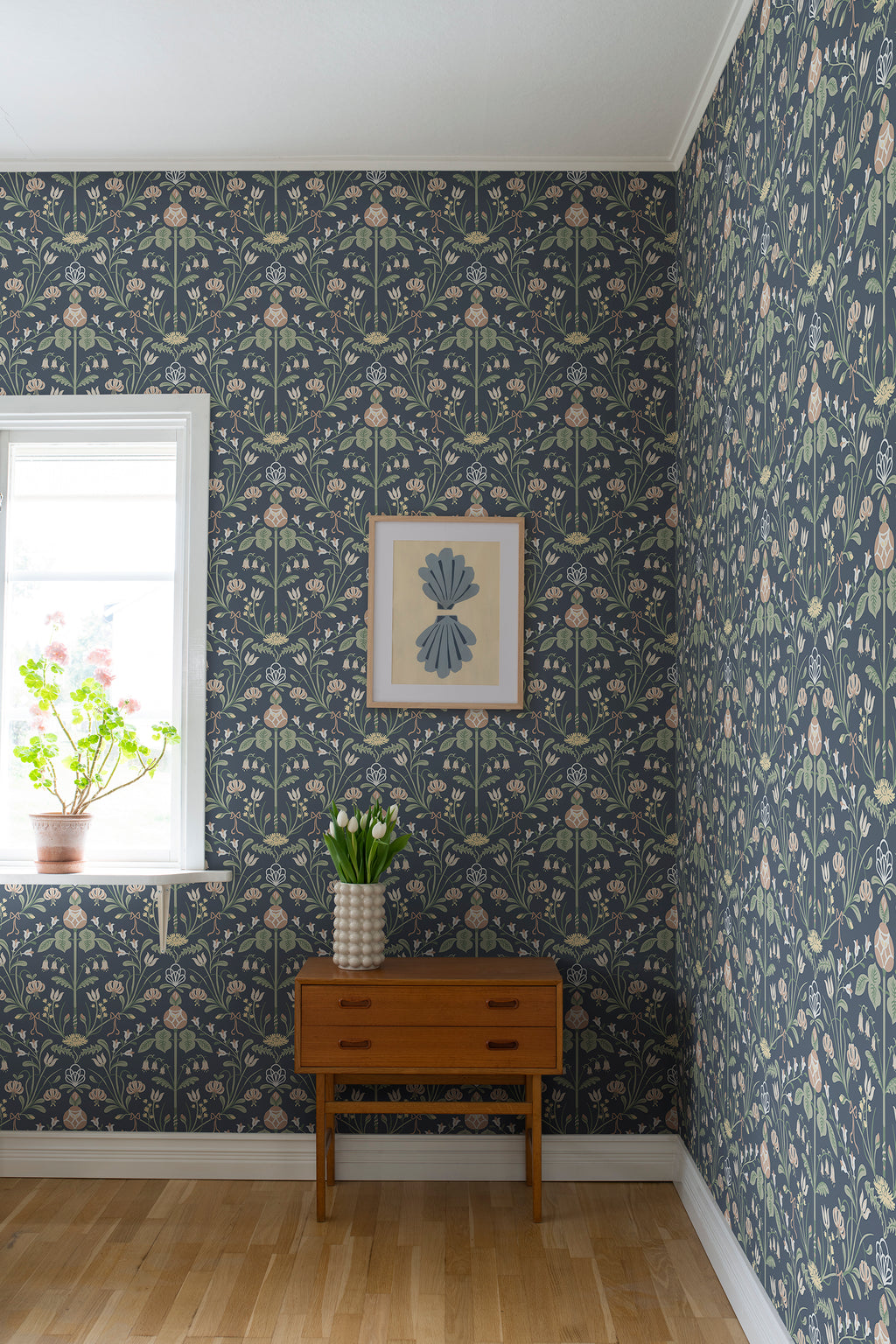 Till Carl wallpaper by Sandberg in navy, styled in a room corner with teak chest and framed art