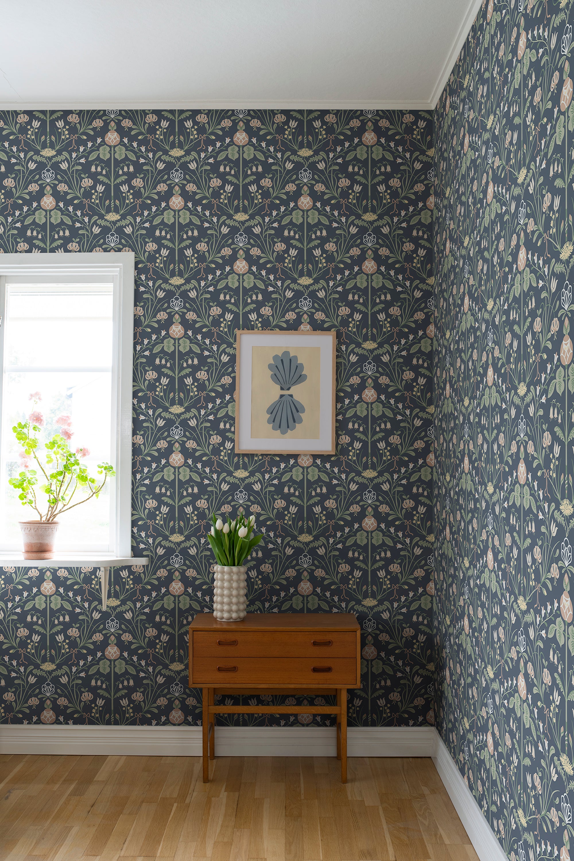 Till Carl wallpaper by Sandberg in navy, styled in a room corner with teak chest and framed art