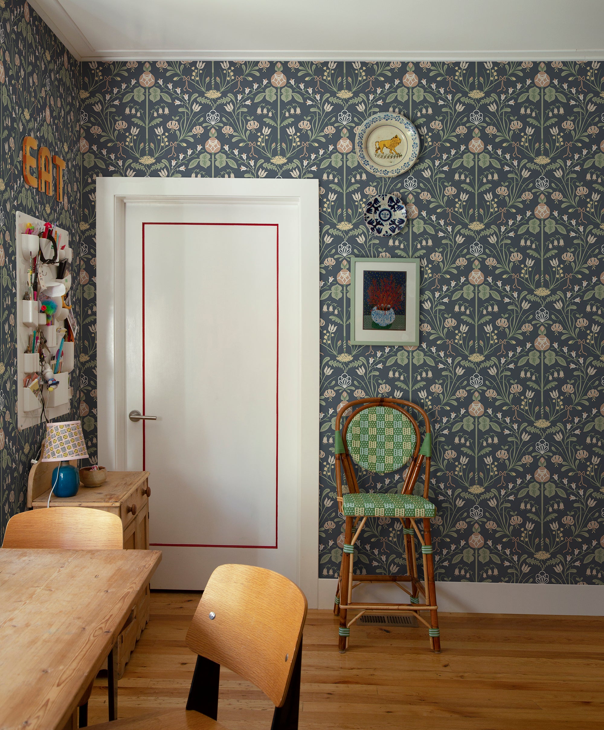 Till Carl wallpaper by Sandberg in navy, in a dining nook beside a white door with rattan chair