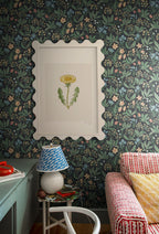 Huset i Solen wallpaper by Sandberg behind a scalloped-framed botanical print, lamp and striped sofa in a styled corner