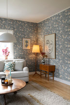 Till Karin wallpaper by Sandberg in dusty blue floral in a living room with grey sofa, floor lamp and line-art print