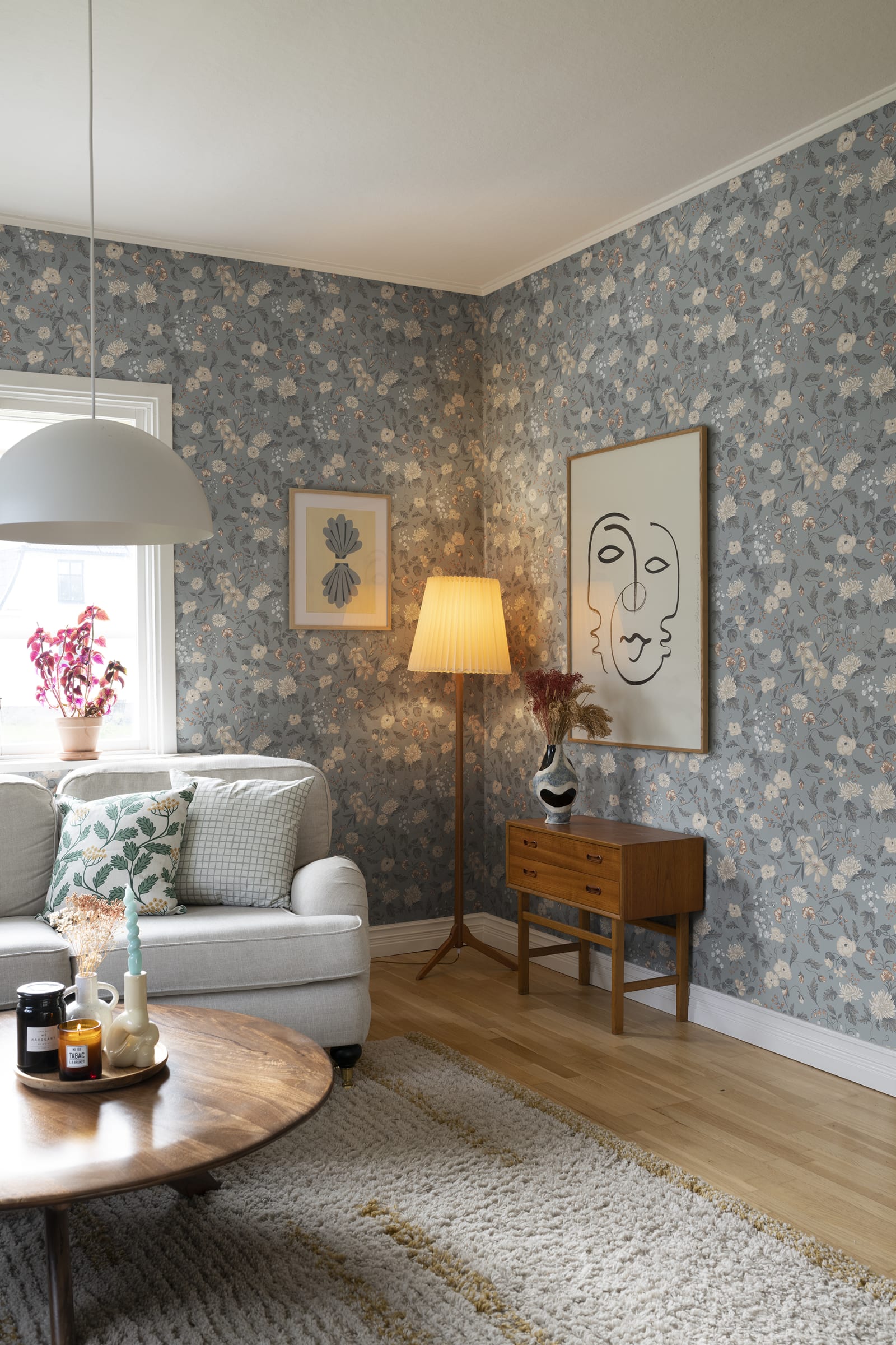 Till Karin wallpaper by Sandberg in dusty blue floral in a living room with grey sofa, floor lamp and line-art print