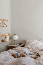 Sigfrid wallpaper by Sandberg in pale grey-cream, styled in a cosy bedroom behind a marble bedside table and brass lamp