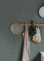 Sigfrid wallpaper by Sandberg in deep green on navy, styled in a kitchen behind a wooden peg rail with apron and produce
