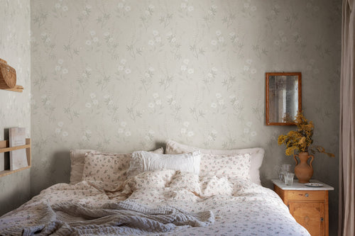 Emma wallpaper by Sandberg in grey-green behind a bed with floral linen and a rustic nightstand