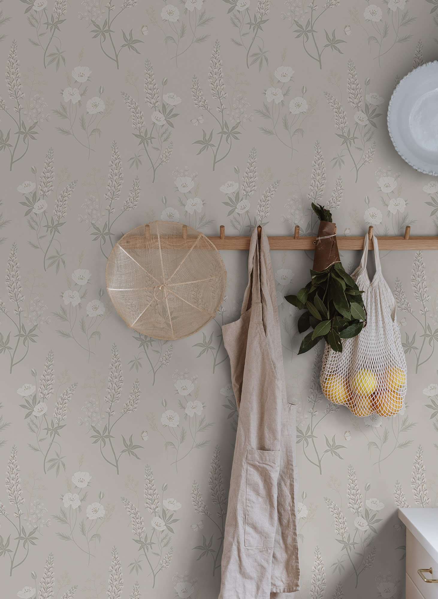 Emma wallpaper by Sandberg in pale grey-green on a wall with peg rail holding an apron and net bag of lemons