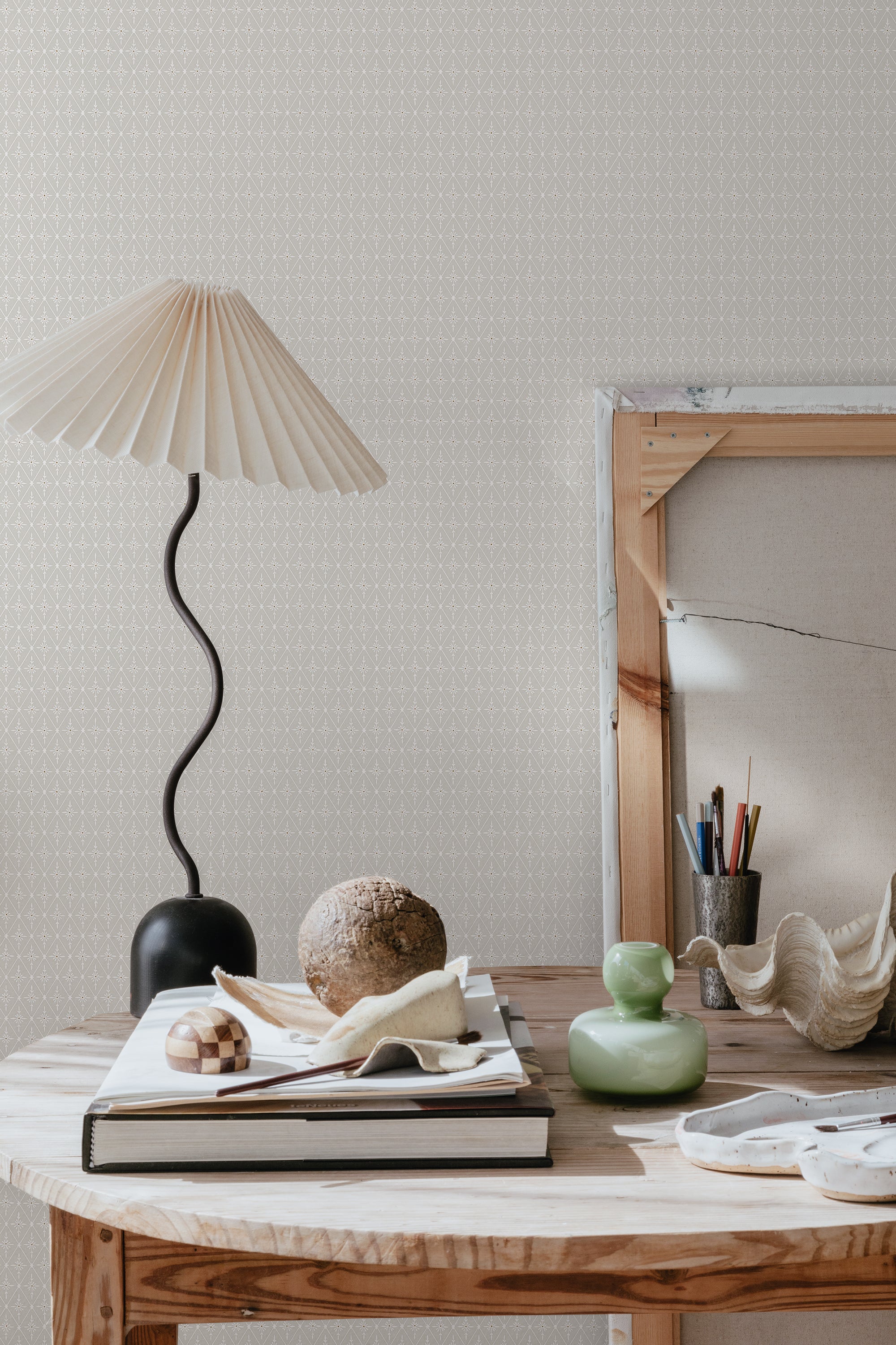 Einar wallpaper by Sandberg in greige on a wall behind a wooden table with pleated lamp and decor