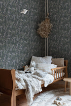 Idun wallpaper by Sandberg in dark green behind a child bed in a nursery with linen and a wooden frame