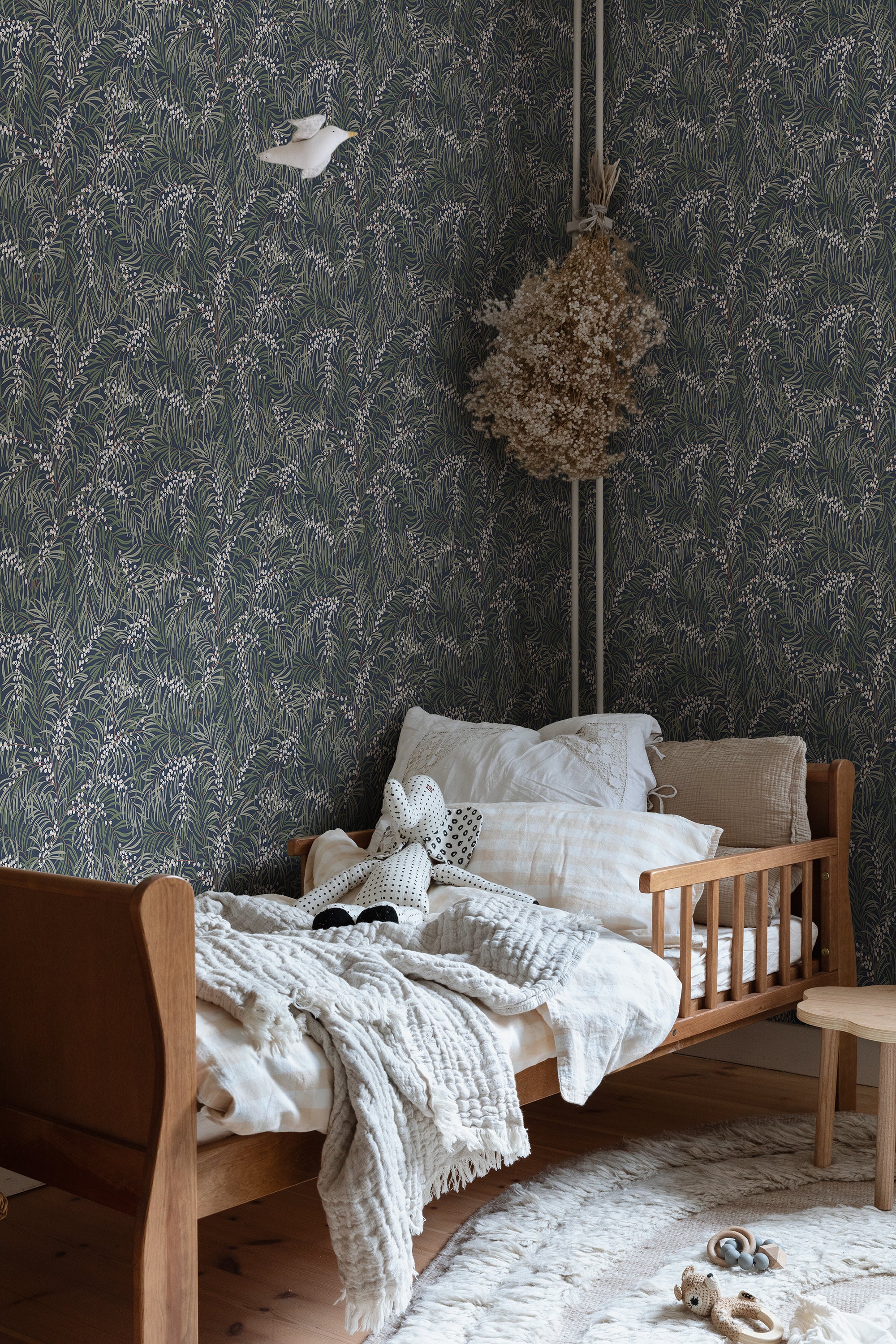 Idun wallpaper by Sandberg in dark green behind a child bed in a nursery with linen and a wooden frame