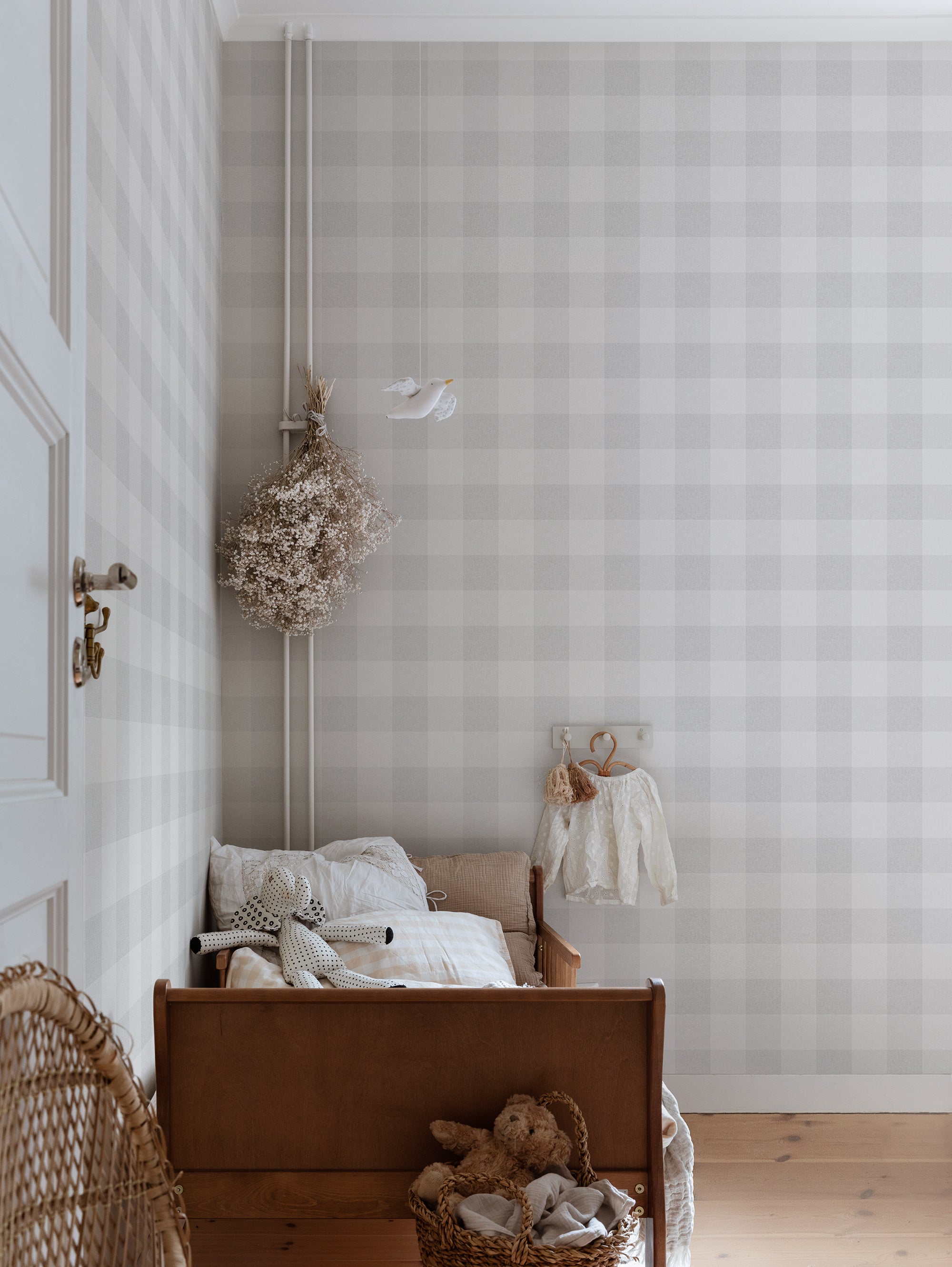 Lykke wallpaper by Sandberg in soft grey check styled in a nursery with a timber cot, dried flowers and a tiny dress