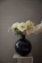 Beata wallpaper by Sandberg as a backdrop, charcoal fan-scallop pattern behind a glossy black vase of cream peonies on a plinth