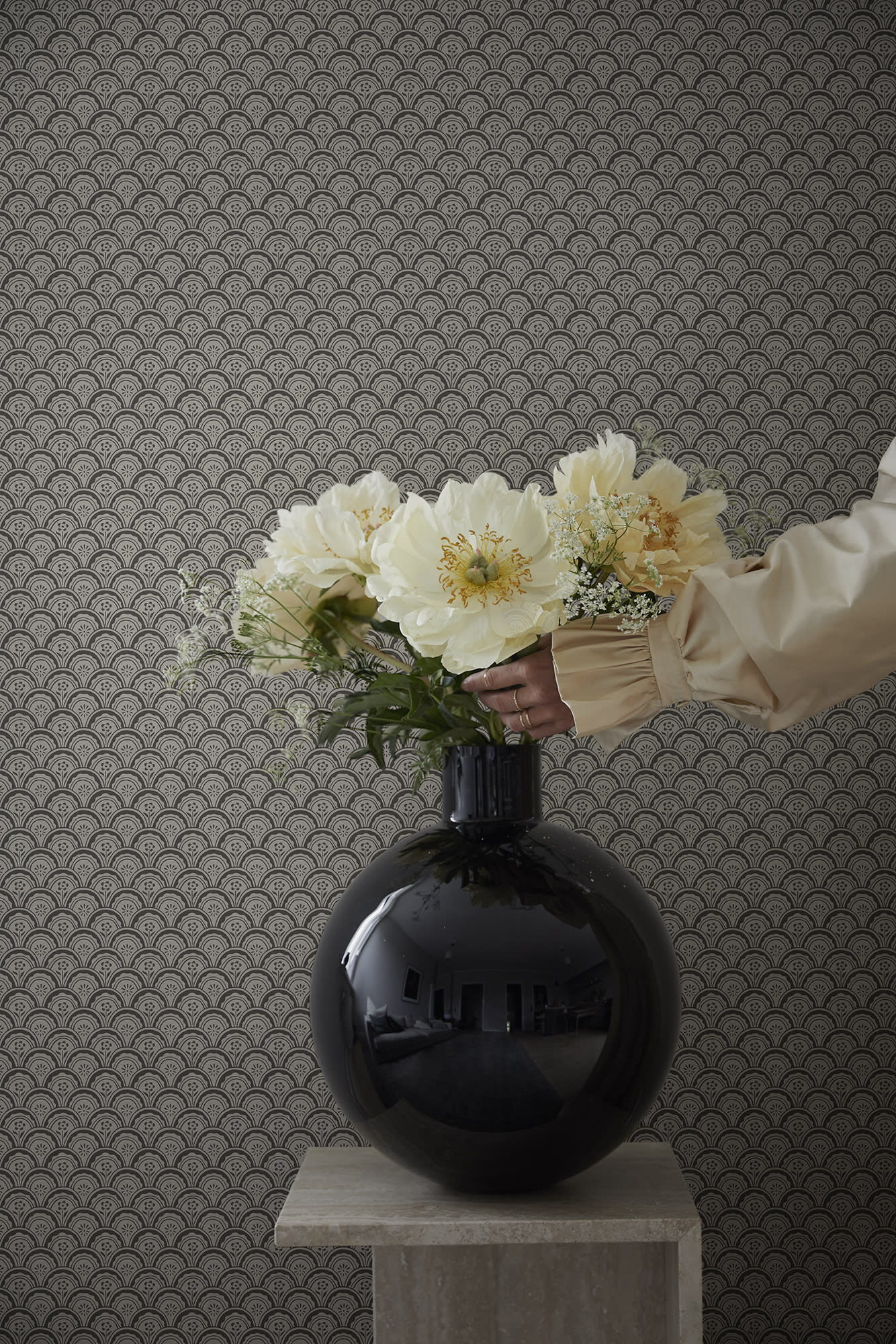 Beata wallpaper by Sandberg as a backdrop, charcoal fan-scallop pattern behind a glossy black vase of cream peonies on a plinth