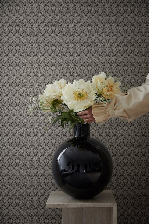 Beata wallpaper by Sandberg as a backdrop, charcoal fan-scallop pattern behind a glossy black vase of cream peonies on a plinth