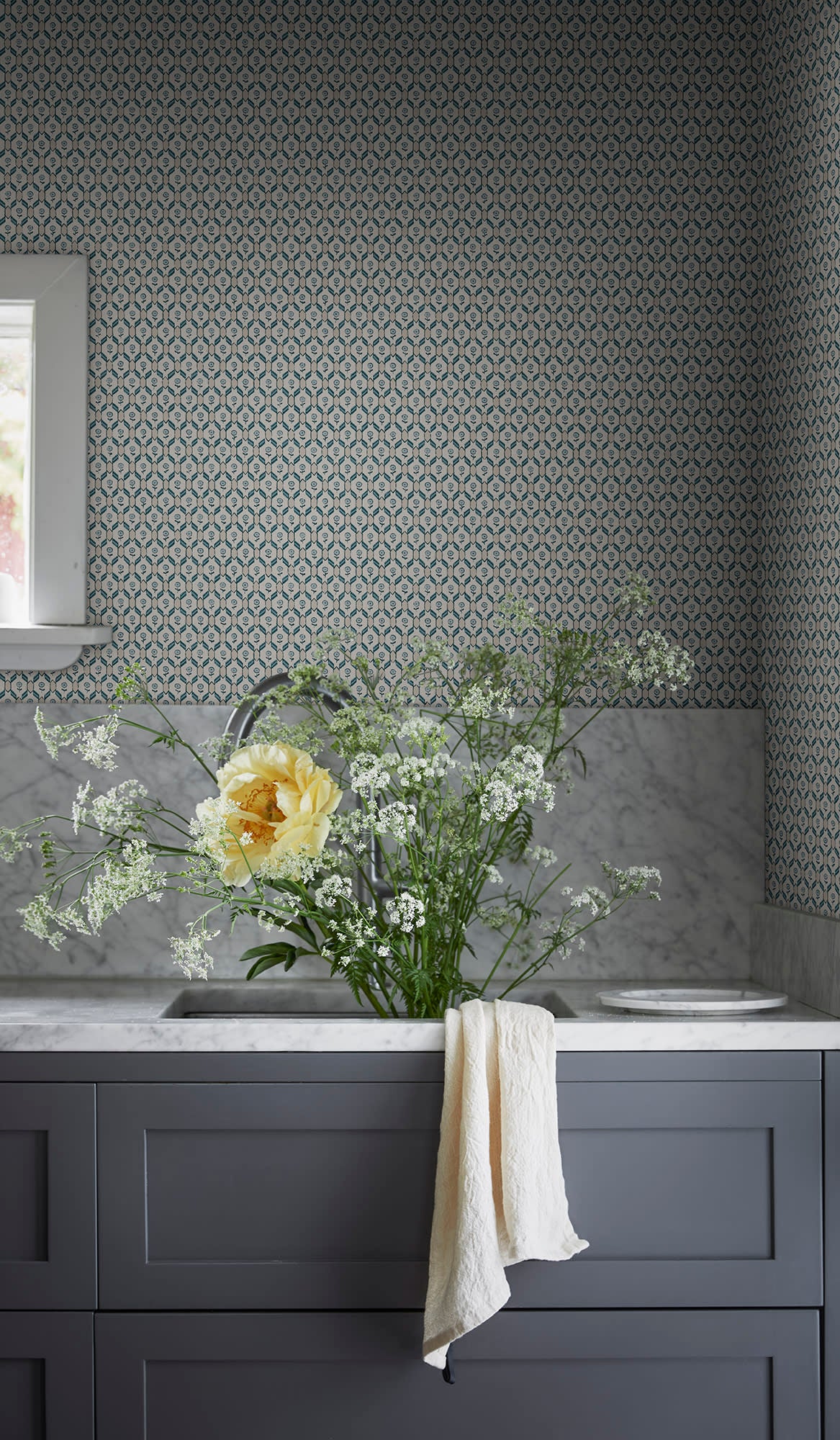 Blue Hugo wallpaper by Sandberg above a marble vanity with grey cabinets and a vase of wildflowers