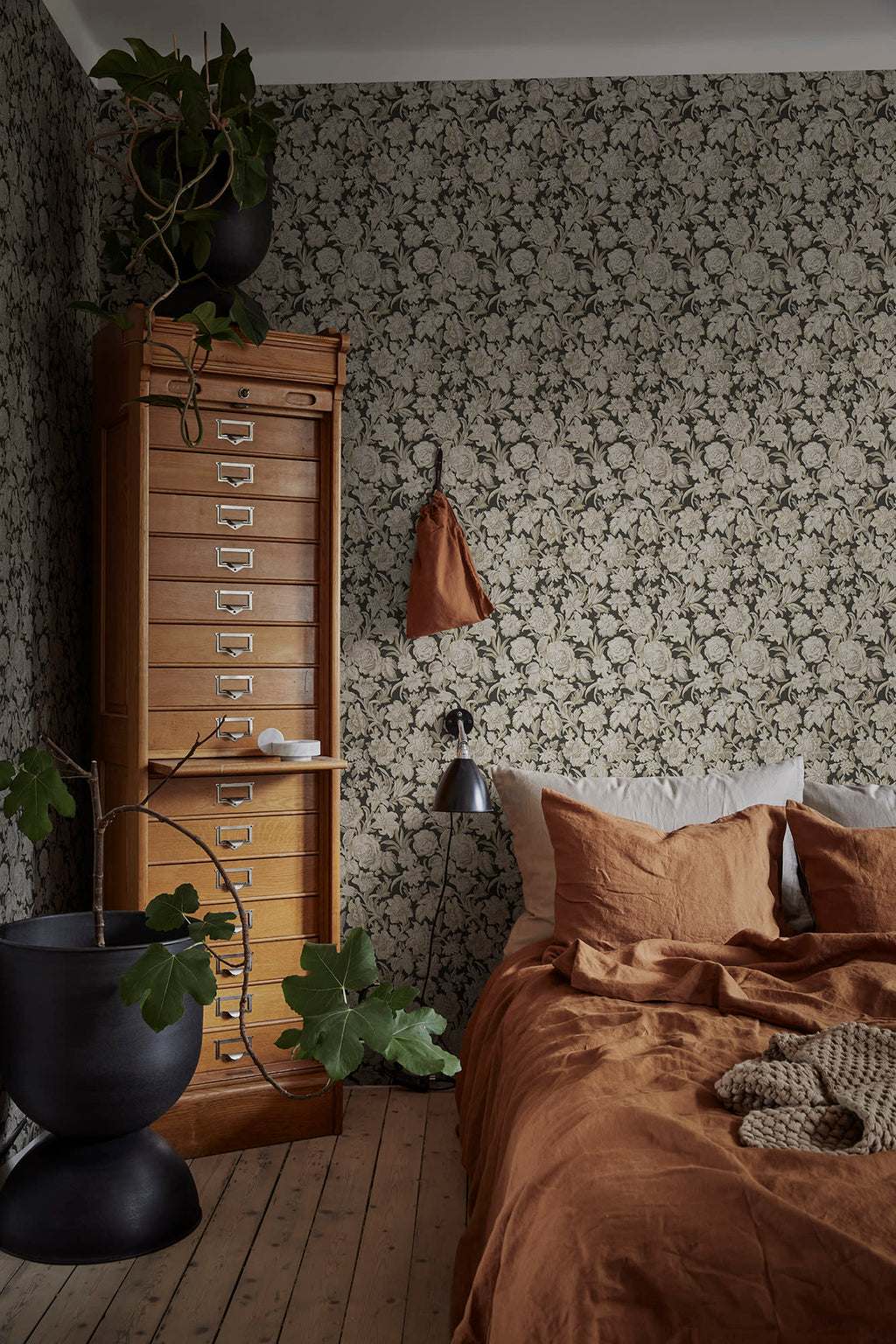 Valentin wallpaper by Sandberg in charcoal in a bedroom with rust linen bedding and a wooden filing cabinet