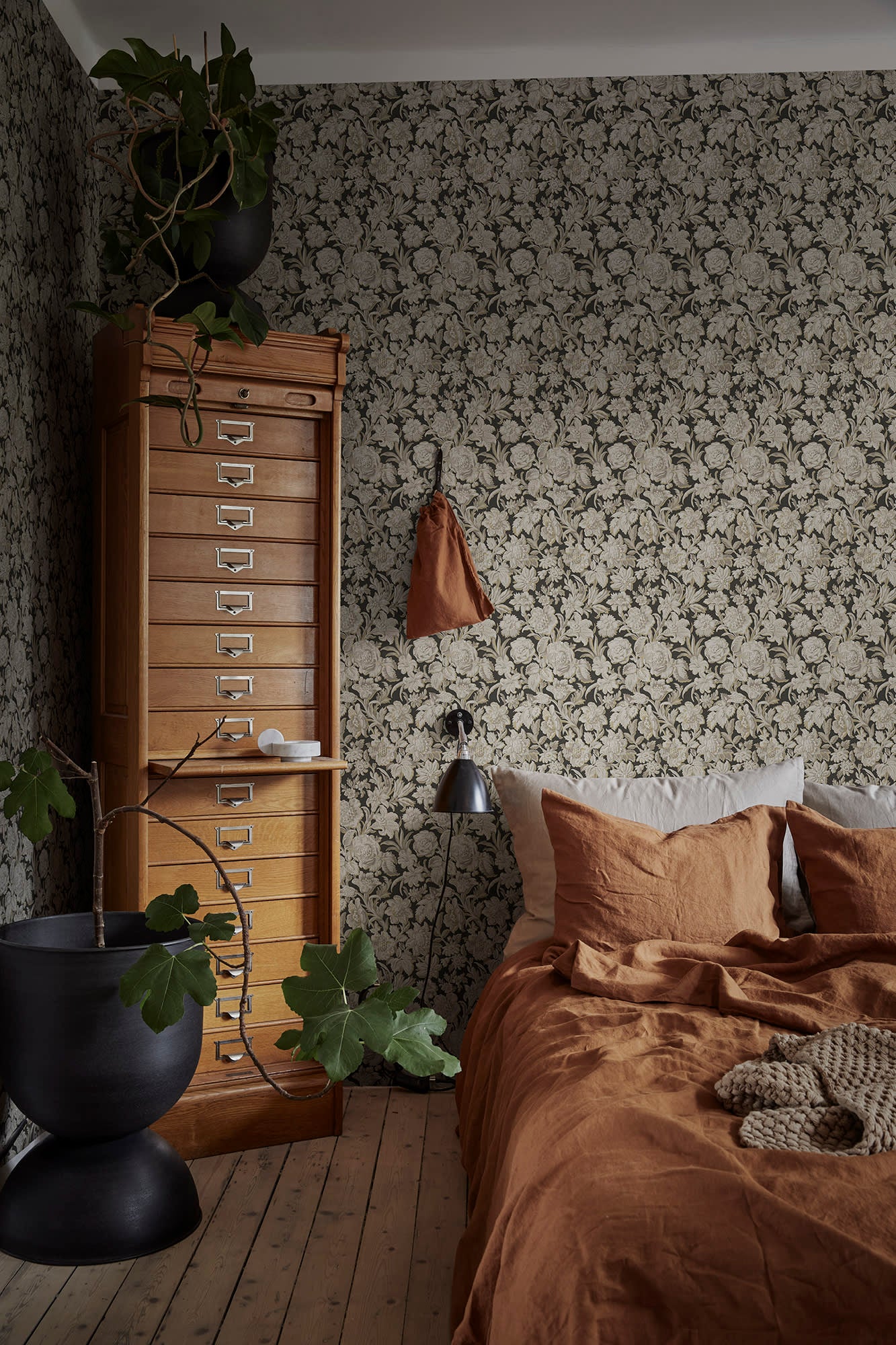 Valentin wallpaper by Sandberg in charcoal in a bedroom with rust linen bedding and a wooden filing cabinet