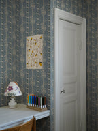Alexandra wallpaper by Sandberg in dusty blue in a study nook with an alphabet print, lamp and pencils by a white door