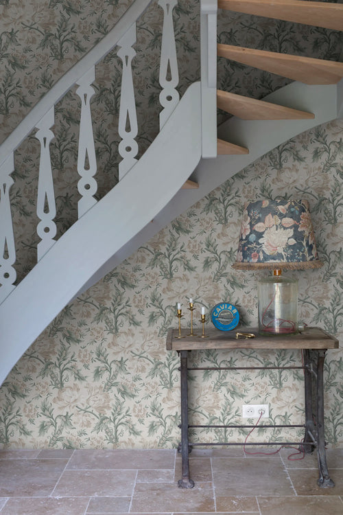Amelia wallpaper by Sandberg in sage green behind a rustic console table and curved staircase, close interior view