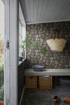 Fig Garden wallpaper by Sandberg in charcoal, in a mudroom with woven basket on a bench and storage crates