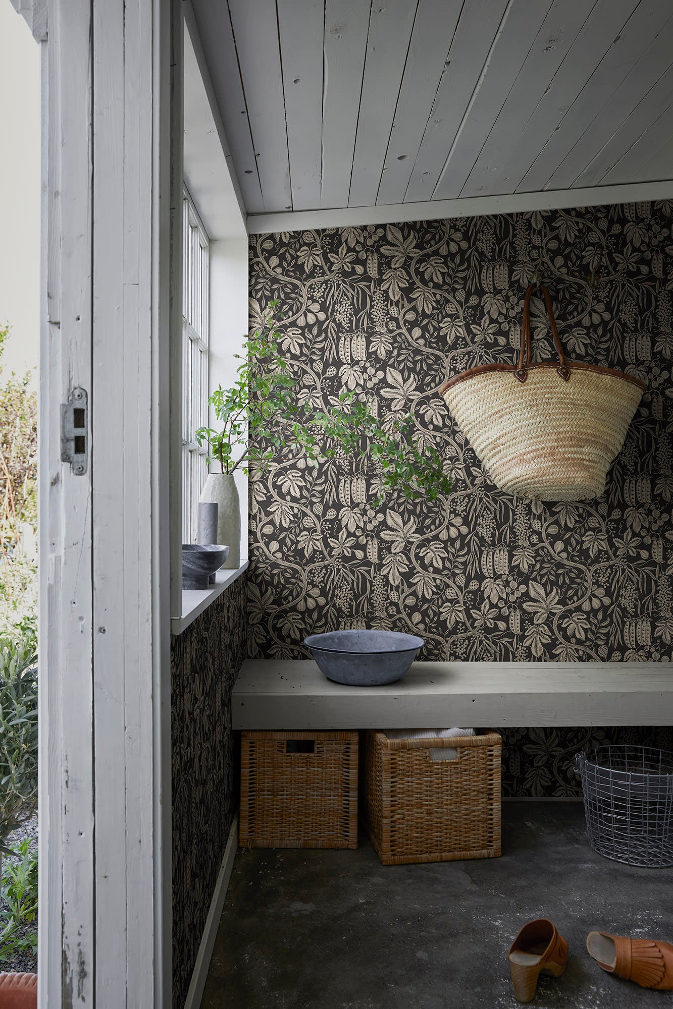 Fig Garden wallpaper by Sandberg in charcoal, in a mudroom with woven basket on a bench and storage crates
