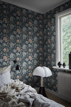 Annabelle wallpaper by Sandberg in dark floral behind a bed in a moody bedroom with a domed lamp and window